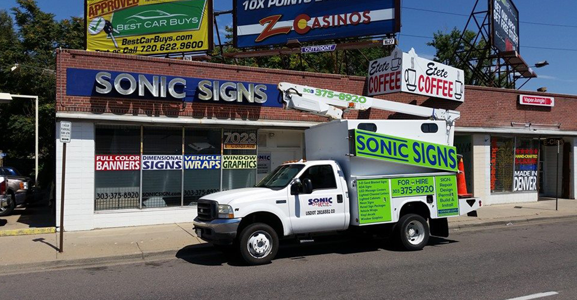 Sonic Signs & Printing storefront with bucket truck and illuminated signs